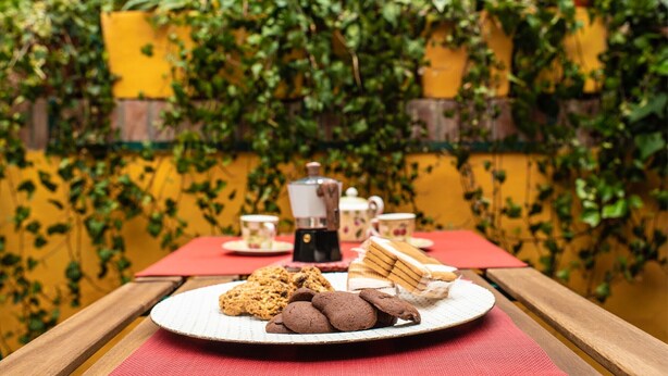 Een picknicktafel met een bord koekjes en sandwiches, een koffiepot en kopjes.
