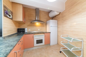 Een keuken met houten kastjes, een magnetron, oven en een witte koelkast.