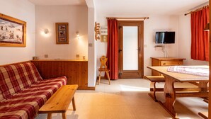 Ein gemütliches Zimmer mit einer Holz-Couch, einem Holztisch, einem Fernseher und einer Tür zu einem weiteren Raum.