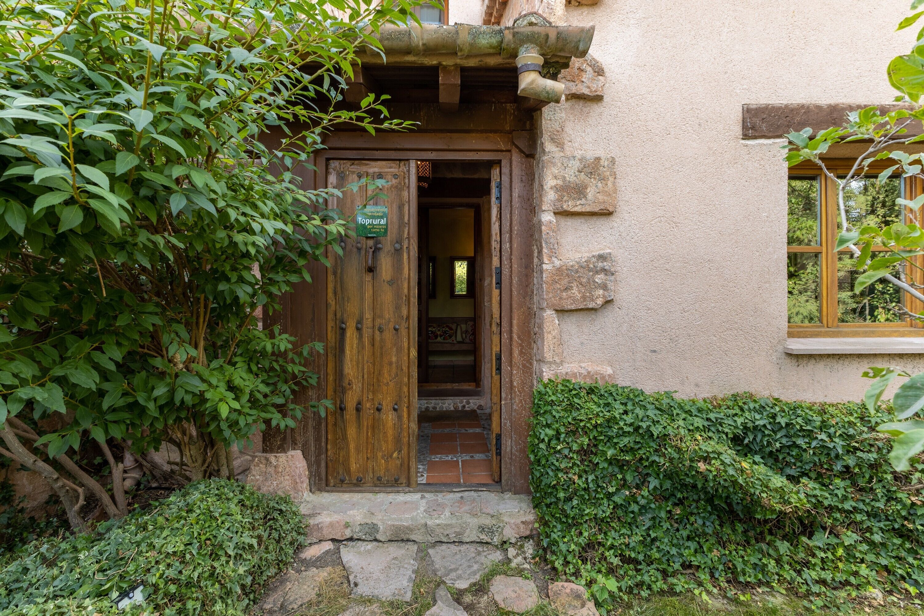 Una puerta de madera rústica con un letrero, un sendero de piedra y un seto verde exuberante.
