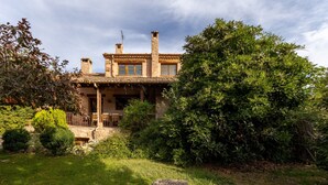 A rustic house with a stone facade, multiple chimneys, and a well-maintained garden. - Dalt La Figuera Country House — Guadarrama, Mountain Views, Pool & Wi-Fi (La Higuera)