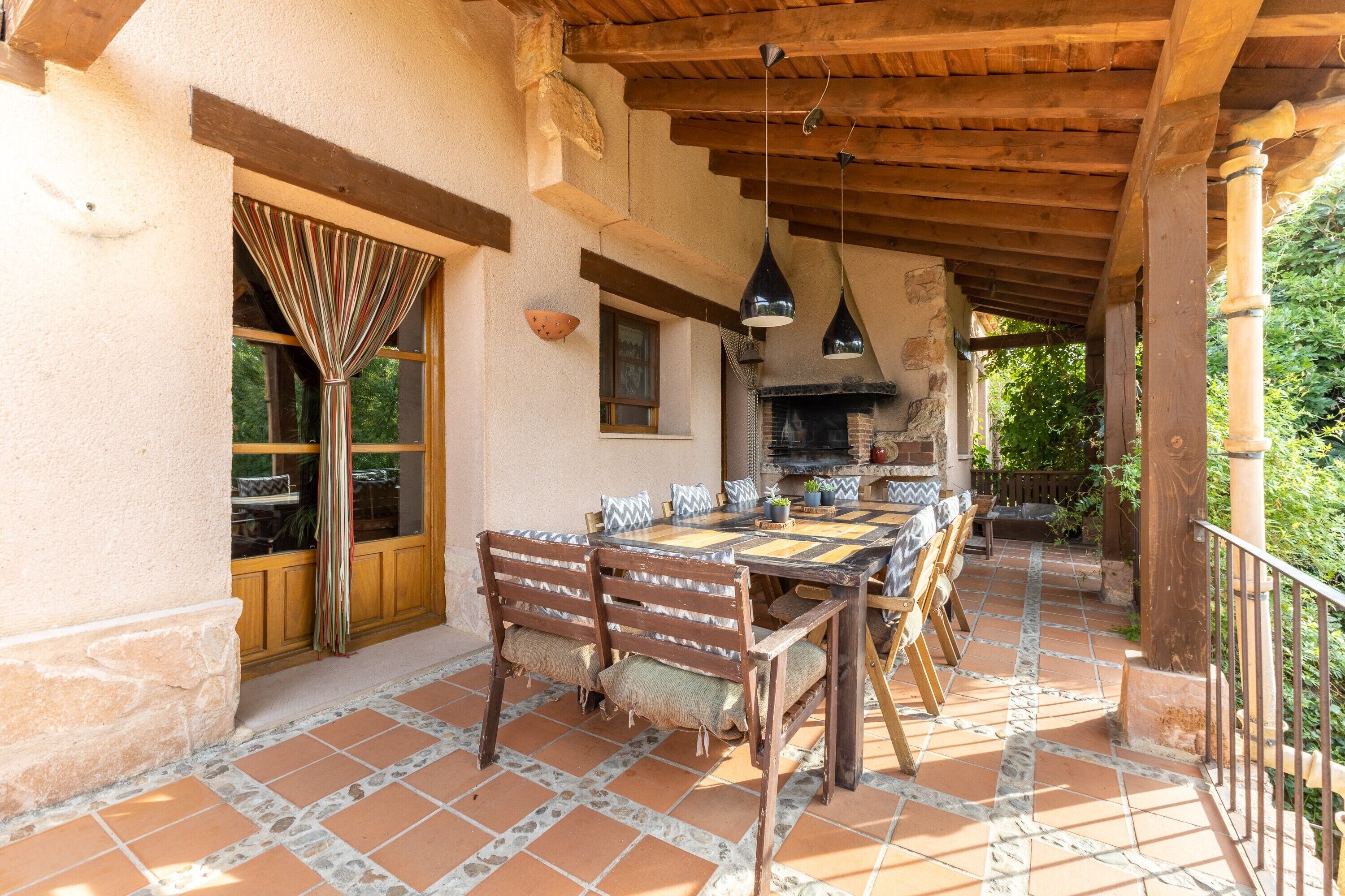 Eine Terrasse im Freien mit einem Holztisch und -stühlen, einem steinbelagten Boden und einer rustikalen Steinwand.