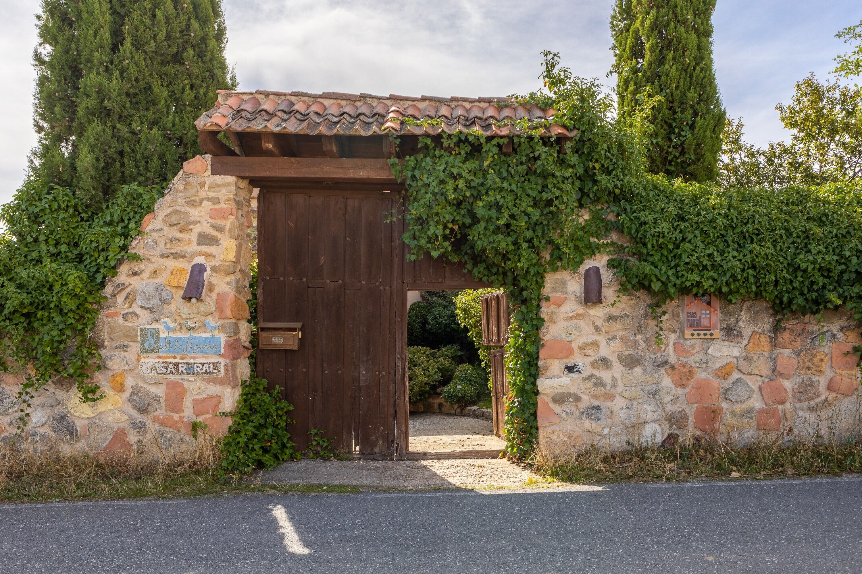 A stone gate with a wooden door, surrounded by greenery and a stone wall.