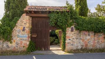 A stone gate with a wooden door, surrounded by greenery and a stone wall.