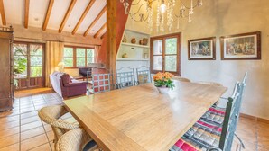 A spacious dining area with a large wooden table, wicker chairs, and a chandelier. - Dalt La Figuera Country House — Guadarrama, Mountain Views, Pool & Wi-Fi (La Higuera)