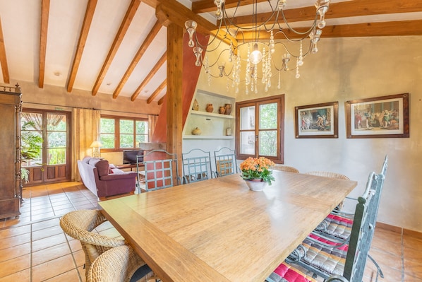A spacious dining area with a large wooden table, wicker chairs, and a chandelier.