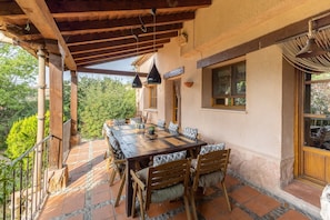 An outdoor patio with a wooden table and chairs, surrounded by stone tiles and a wooden pergola.