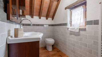 A compact bathroom with a wooden vanity, a white sink, a toilet, and a small window with a curtain.