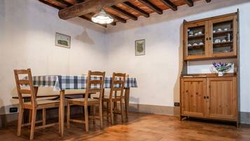 Uma sala de jantar com mesa e cadeiras de madeira, um armário com portas de vidro e chão ladrilhado.