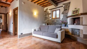 Ein Wohnzimmer mit Sofa, Kamin, Steinwänden, Holzbalken und einem Steinumbau für den Kamin.