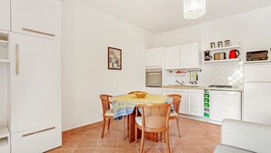 A kitchen with white cabinets, a dining table with chairs, a hanging light fixture, and a tiled floor. - Apartment 'Bel 4p St-Maxime' with Private Terrace, Garden, and Wi-Fi (Sainte-Maxime)