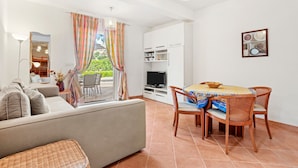 A modern living room with a sofa, dining table, chairs, a TV, and a balcony with curtains. - Apartment 'Bel 4p St-Maxime' with Private Terrace, Garden, and Wi-Fi (Sainte-Maxime)