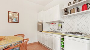 A kitchen with white cabinets, a stove, a sink, and a dining area with a table and chairs. - Apartment 'Bel 4p St-Maxime' with Private Terrace, Garden, and Wi-Fi (Sainte-Maxime)