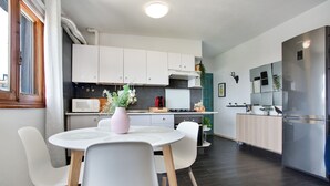 Ett modernt kök med vita skåp, ett kylskåp i rostfritt stål och en matplats med ett vitt bord och stolar.