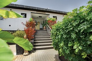 Un edificio con una escalera que conduce a una puerta, rodeado de follaje y una estatua.