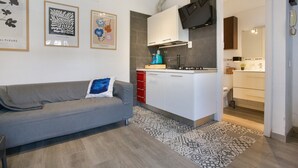 Una cocina moderna con armarios blancos, horno empotrado y sofá gris con un cojín azul.