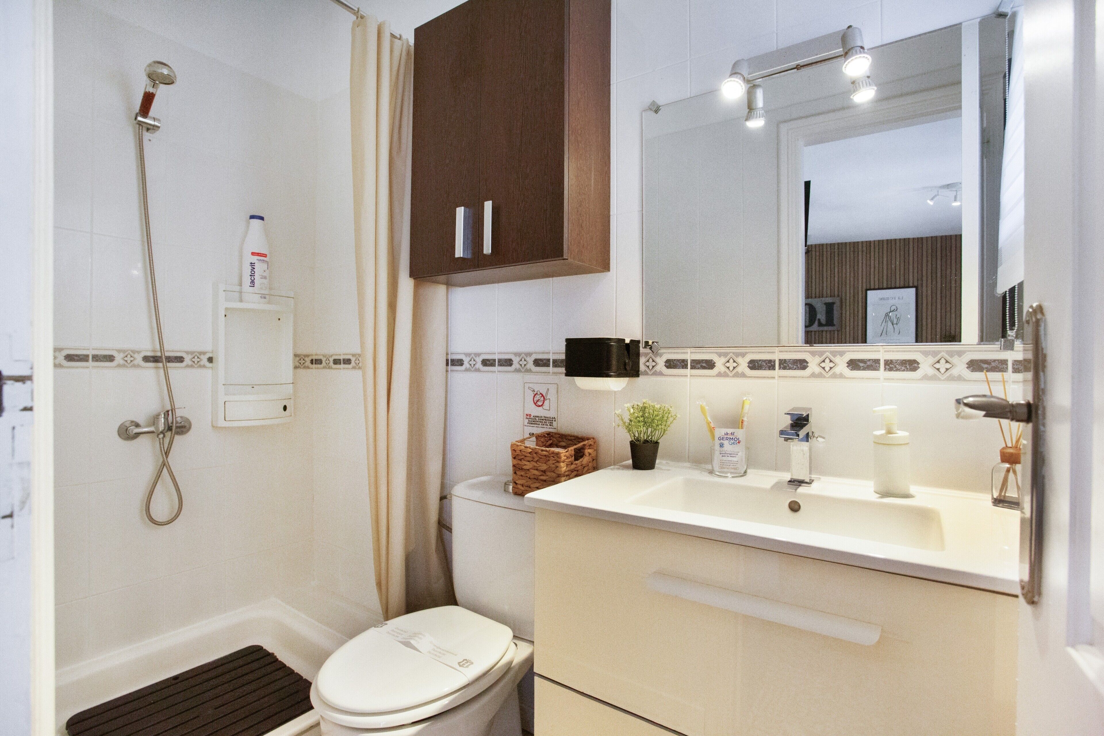 Een badkamer met douche, toilet, wastafel en spiegel.