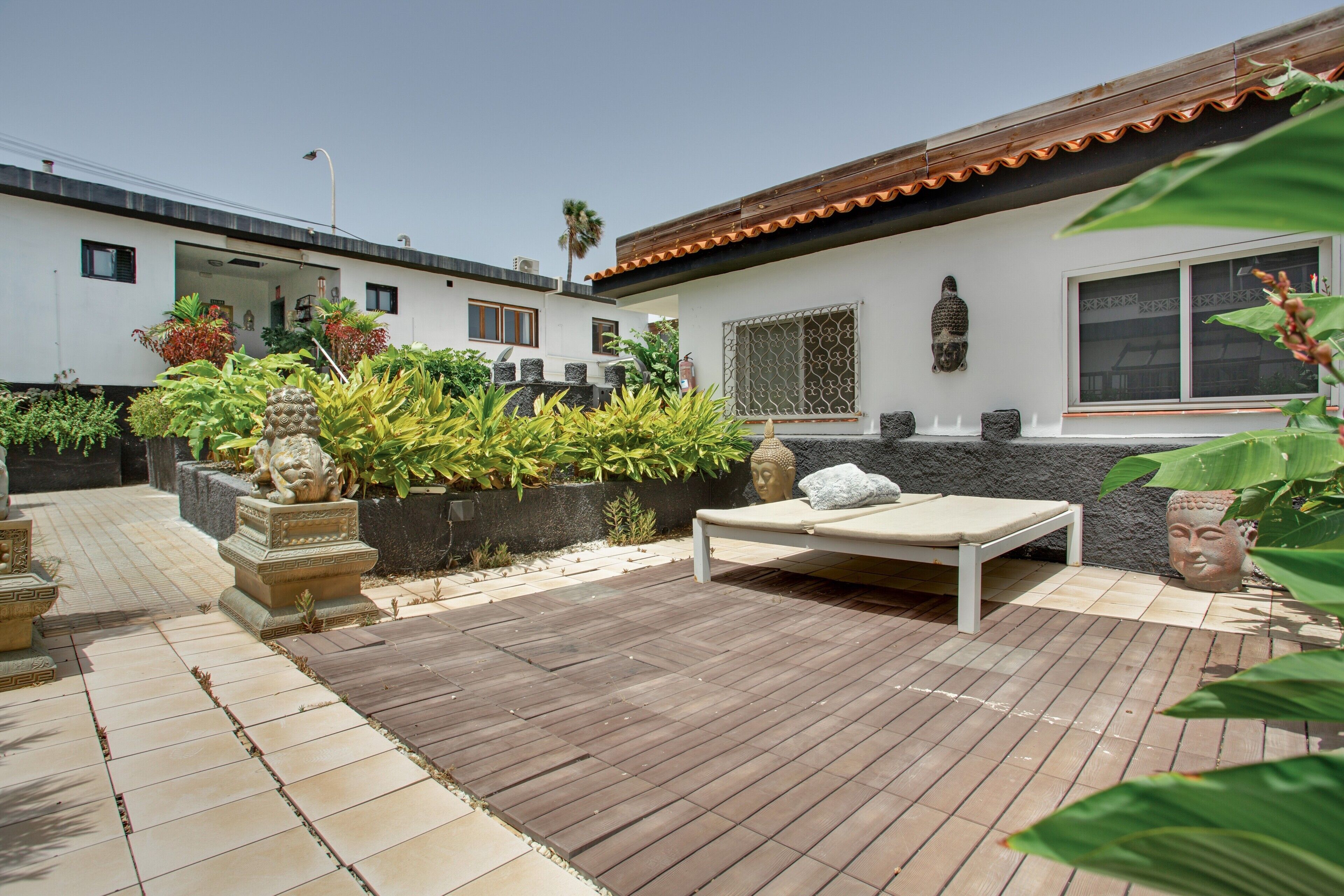 Un patio con un pavimento in legno, un muro bianco con una finestra e una statua di Buddha.