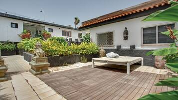 Un patio con un pavimento in legno, un muro bianco con una finestra e una statua di Buddha.