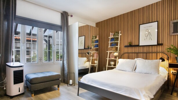 Un dormitorio moderno con cama, mesitas de noche, un calentador, un banco, un armario y una ventana con cortinas.