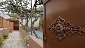 Een binnenplaats met betegelde vloer, potplanten, een pergola en een decoratieve deur.
