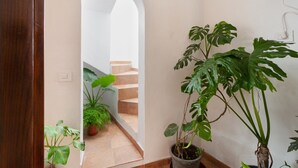 Een gang met een houten deur, een plant in pot, een trap en een witte muur.