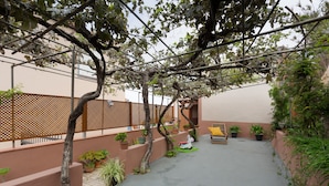 Een overdekte buitenruimte met een houten bank, plantenpotten en een pergola.