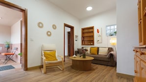 Een woonkamer met een bank, fauteuil, bijzettafeltje en decoratieve wandkunst.