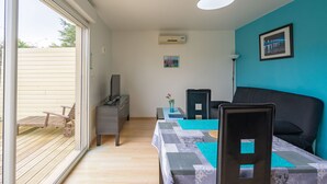 Quarto com cama, escrivaninha, cadeira, mesa com toalha de mesa estampada, vaso com flores e um quadro na parede.