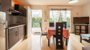 Cozinha compacta com eletrodomésticos modernos, área de refeições com toalha de mesa xadrez e uma televisão sobre suporte.