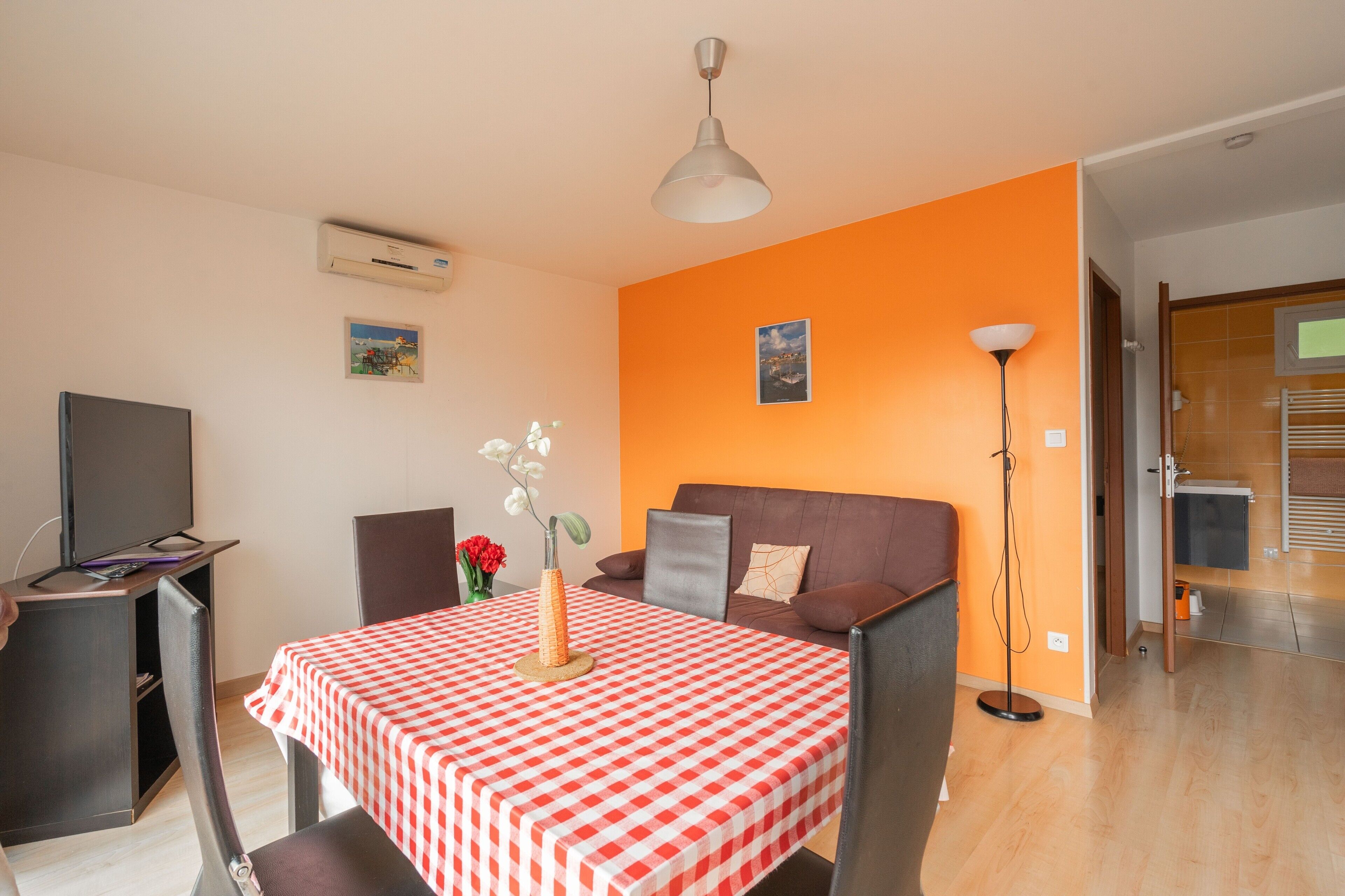 Ein Zimmer mit kariertem Tisch, einer Couch, einem Fernseher und einer Klimaanlage.