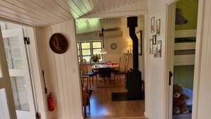 Un pasillo con piso de madera que conduce a un comedor con mesa, sillas y un reloj. Se ve un osito de peluche en una habitación infantil.
