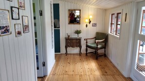 Habitación con piso de madera, una silla tapizada de verde, un armario de madera y un espejo en la pared.