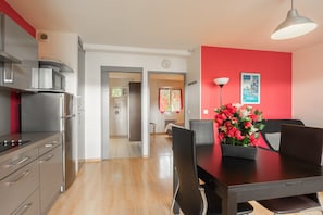 A modern kitchen with stainless steel appliances, a dining area with a black table and chairs, and a red accent wall.