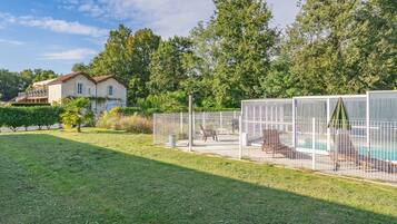 A fenced outdoor area with a pool, a house in the background, and a grassy lawn.