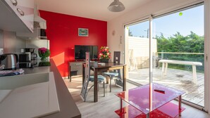 Eine moderne Küche mit roter Akzentwand, eine Essecke mit Tisch und Stühlen sowie ein Balkon mit Blick auf Grünflächen.