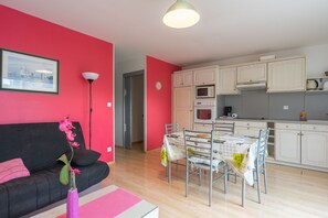 Eine moderne Küche mit weißen Schränken, einem Esstisch mit Stühlen und einem schwarzen Sofa mit einer rosafarbenen Vase.