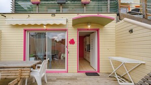 Una terraza de madera con una mesa y sillas, una mesita blanca y una puerta que da a una habitación.