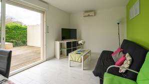 Ein Wohnzimmer mit Sofa, Couchtisch, Fernseher auf einem Schrank und einer Schiebetür zu einem Außenbereich.