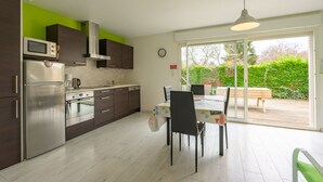 Eine moderne Küche mit Edelstahlgeräten, eine Essecke mit Tisch und Stühlen sowie eine Glastür, die auf eine Außenpatio führt.