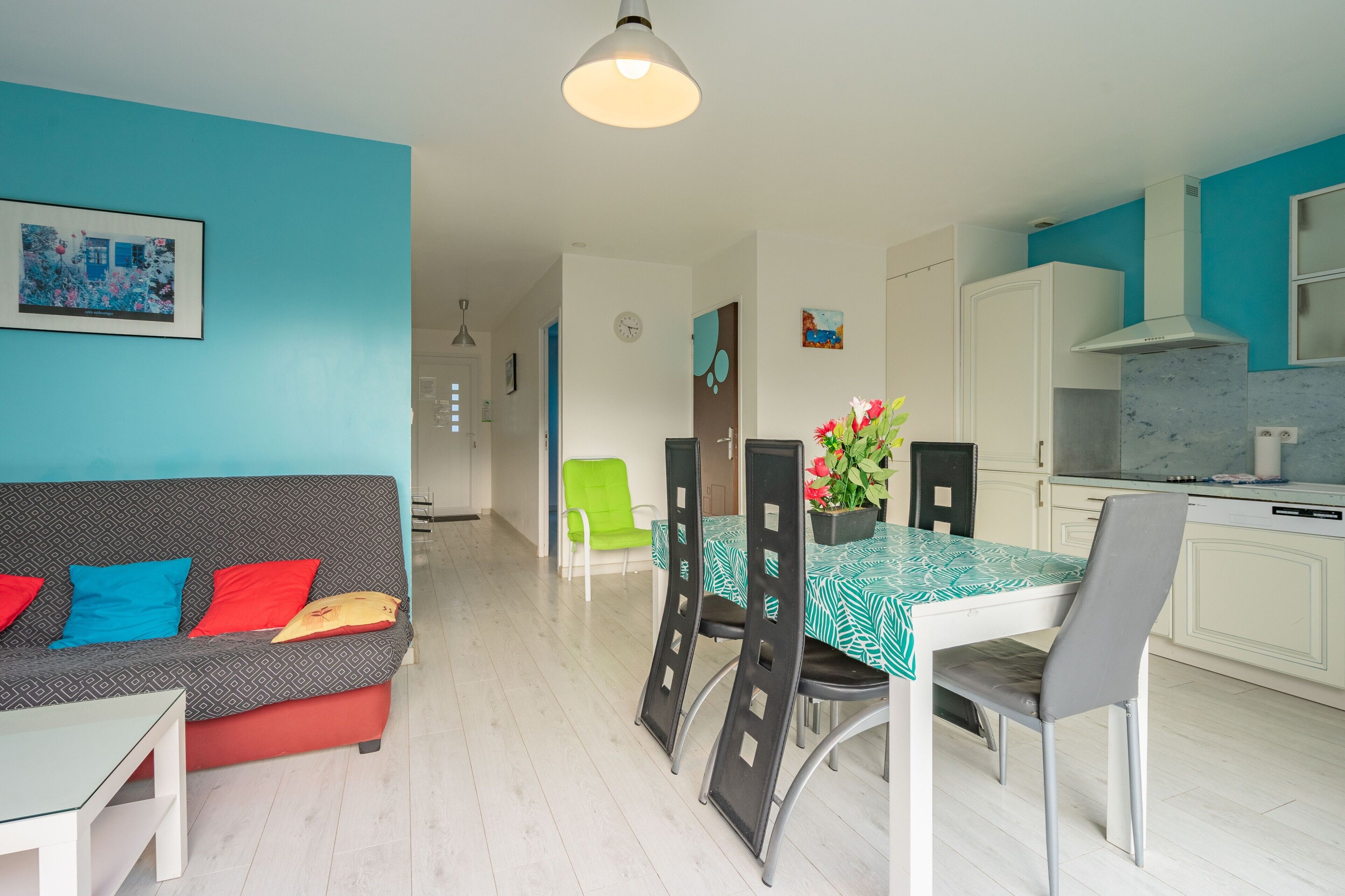 A modern living room with a sofa, dining table, chairs, and a kitchen area with cabinets and a stove.