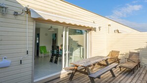 Eine Holzterrasse mit Picknicktisch und -stühlen, eine Schiebetür zu einem Innenbereich und einer kleinen Außenleuchte.