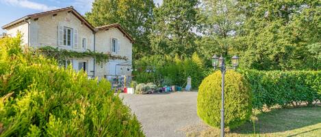 A stone building with a gravel driveway, surrounded by lush greenery and a well-maintained garden.