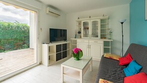 Ein Wohnzimmer mit einer Couch, einem Couchtisch, einem Fernseher, einem Schrank und Blick ins Grüne.