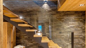 A modern staircase with glass railings and wooden steps, leading to a room with a stone wall and a small white fluffy object on the floor. - Chalet 'Isabella Lodge Pyrénées' with Lake View, Private Terrace and Wi-Fi (Bolquere Pyrenees 2000)