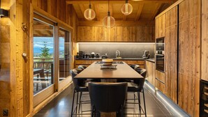 A modern kitchen with wooden walls, a large dining table, and pendant lights. - Chalet 'Isabella Lodge Pyrénées' with Lake View, Private Terrace and Wi-Fi (Bolquere Pyrenees 2000)