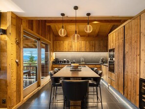 A modern kitchen with wooden walls, a large dining table, and pendant lights.
