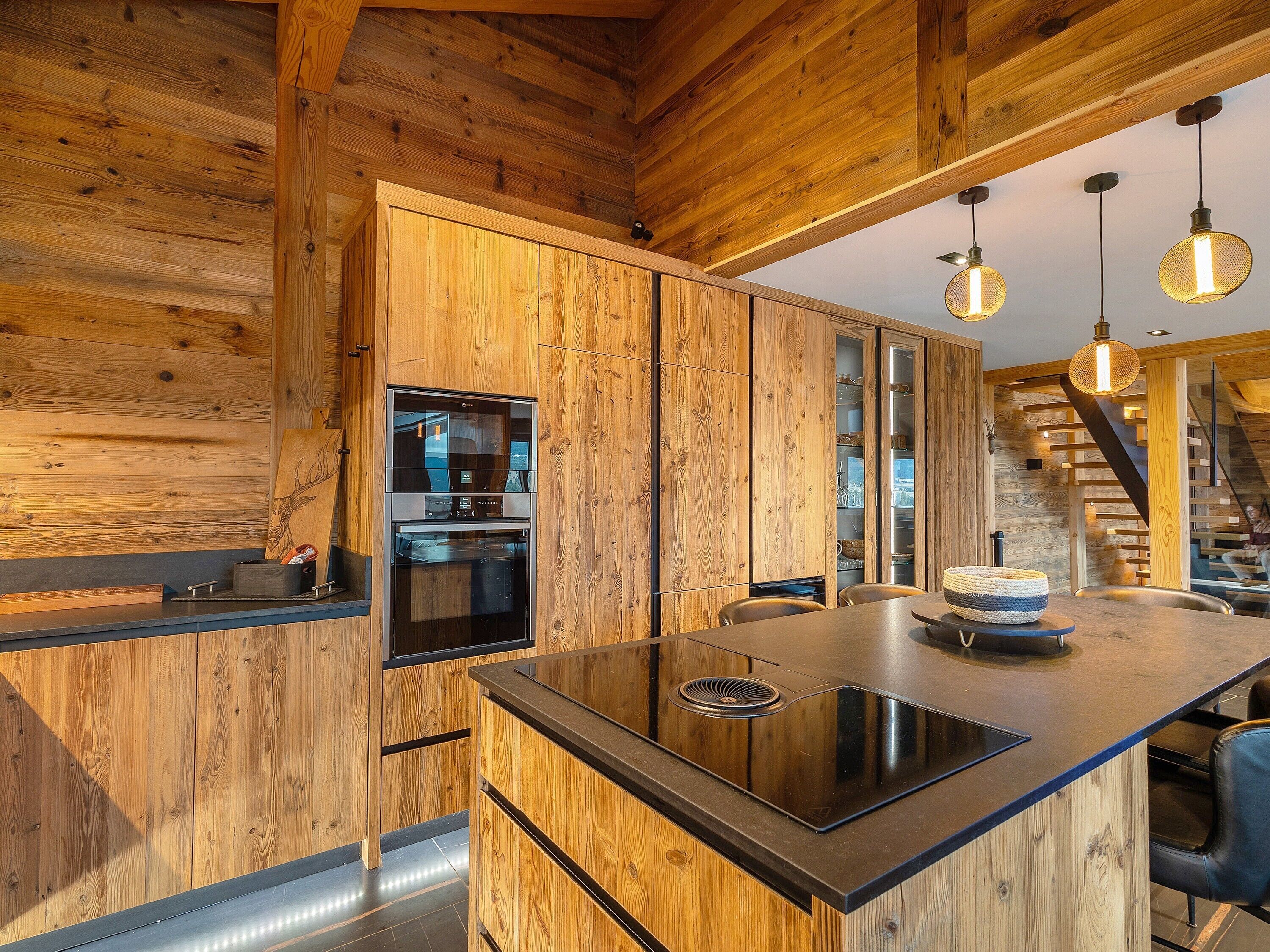 Una cocina moderna con armarios de madera, horno empotrado y una isla central con encimera negra.