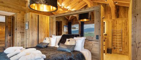 A wooden interior with a bed, towels, and a view through a window.