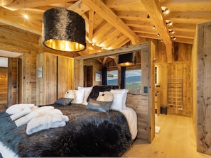 A wooden interior with a bed, towels, and a view through a window.